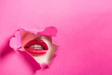 cropped image of seductive girl showing lips in hole in pink paper