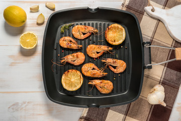 Grilled shrimps on a grill frying pan with lemon, paprika, spices and herbs. Wooden background.