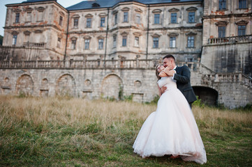 Obraz premium Fabulous wedding couple posing in front of an old medieval castle in the countryside on a sunny day.
