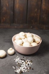 Diet, Italian Food Cooking, Vegetarian Concept. A bowl of fresh button mushrooms and sea salt grains and black pepper corns on a black table against a dark wooden wall