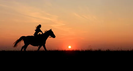 Foto op Plexiglas Te paard vrouw rijden op galopperend paard met rode rijzende zon aan de horizon. Mooie kleurrijke zonsondergang achtergrond met paarden en meisjes silhouet paard wandelen © Max