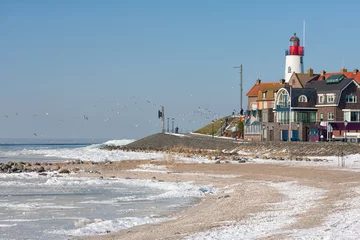 Cercles muraux Phare Winter landscape with Dutch beach covered with snow and view at lighthouse of fishing village Urk