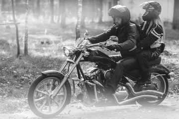 Fototapeta na wymiar Young romantic couple in a forest road on a motorcycle. Love, freedom, togetherness concept. Happy guy and girl travel on a motorbike, road trip adventure concept black and white