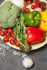 Diet, Healty Food Cooking, Vegetarian Concept. A plate of fresh raw vegetables: cherry tomatoes, broccoli, paprika peppers, rosemary, garlic and spices on a dark table, top view