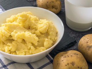 Puree. Mashed potatoes in a white plate, fresh potato, milk in a white Cup. Grey background