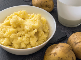 Puree. Mashed potatoes in a white plate, fresh potato, milk in a white Cup. Grey background