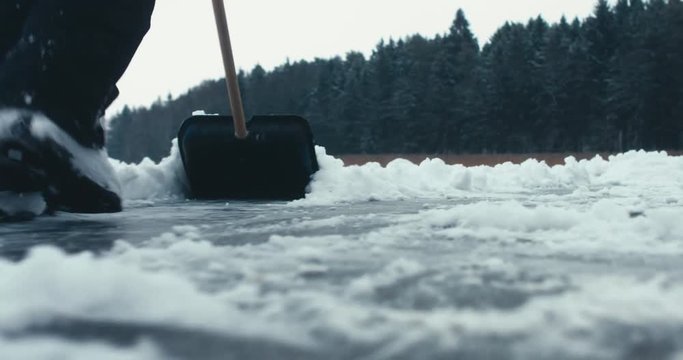 CU Male cleaning lake surface from snow before ice-skating and playing pond hockey. 4K UHD