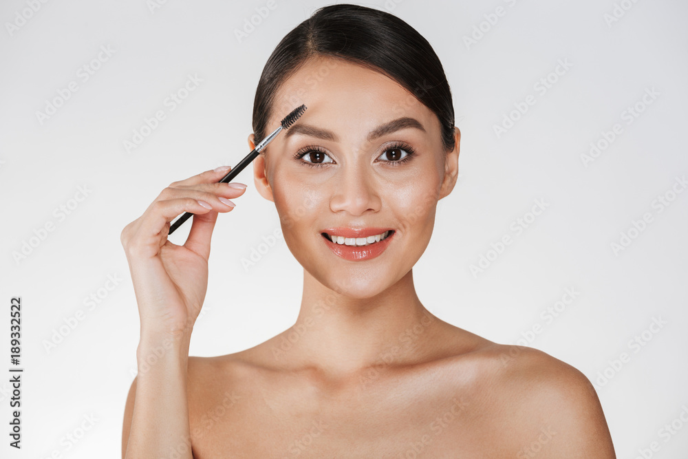 Sticker beauty picture of pretty young woman with hair in bun looking on camera and combing her eyebrows wit