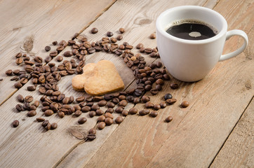 The cup of coffe and Frame- heart from coffee beans and two cookies-heart  inside it on  wooden table