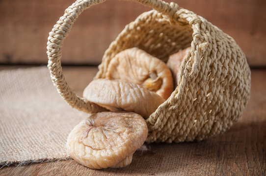 figues s&eacute;ch&eacute;es tombant d'un petit panier en osier sur fond en bois et toile de jutte