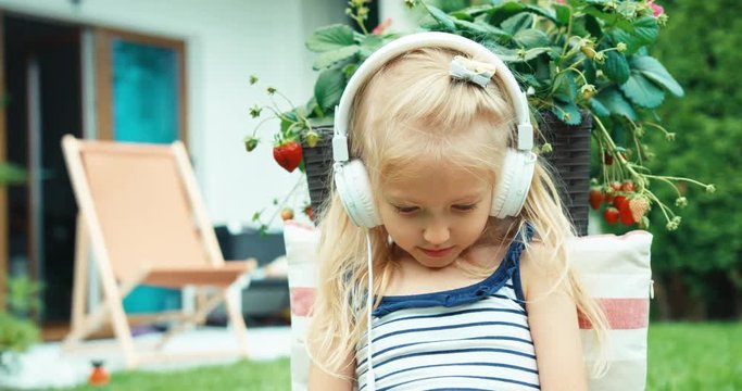 Little blond girl listening music in headphones in the garden