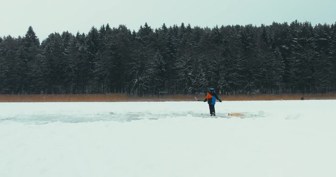 WIDE Kid playing pond hockey on a frozen lake alone. 4K UHD