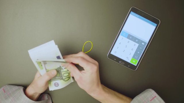 Top view. Male hands counts money and summarize the result on the calculator. Text on the tablet - calculator