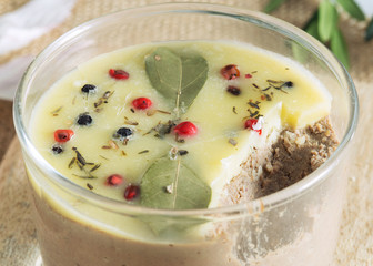 Clos up of Chicken liver pate jar covered with melted butter and decorated with bay leaves and black and red pepper.