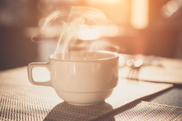 Hot coffee on old wood table with smoke and blur background of sunlight shining,  soft focus