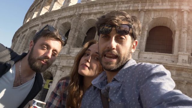 CAMERA POV Three happy young friends tourists with bikes and backpacks at Colosseum in Rome taking selfies pictures with smartphone and stick having fun on sunny day slow motion
