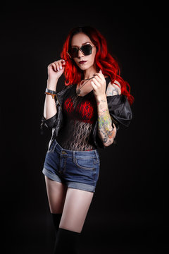 Close up of beautiful woman with tattoo wearing jeans short paint against black background.