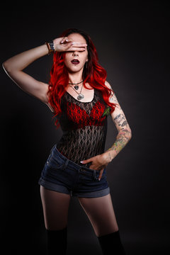Close up of beautiful woman with tattoo wearing jeans short paint against black background.