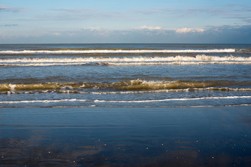 seascapes of coastline with foaming waves on the sea, dark sand and clouds on the horizon