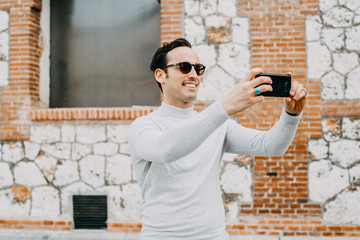 .handsome young man using his mobile phone, taking pictures with happy face outdoors on a sunny autumn day. Lifestyle.