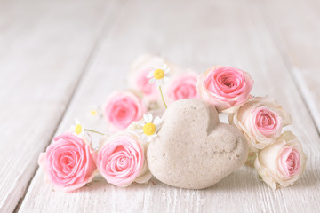 Pink roses and stone heart on rustic wooden background