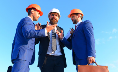 Builders discussing plan and argue, blue sky background.