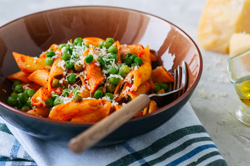 Tomato sauce and green peas penne pasta in a plate on a white stone background