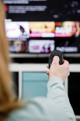 Woman Holding a TV remote control and switching channels on TV set