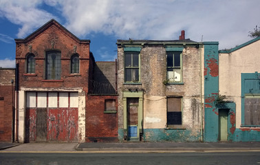 derelict houses and abandone garage on a residential street with boarded up windows and decaying...