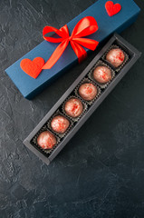Blue gift box with red tape with chocolate on a black stone background