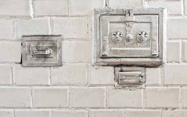 Closed metal door of an old white tiled stove.