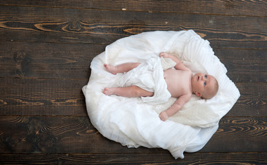 Baby lying on white blanket designed as cloud or nest.