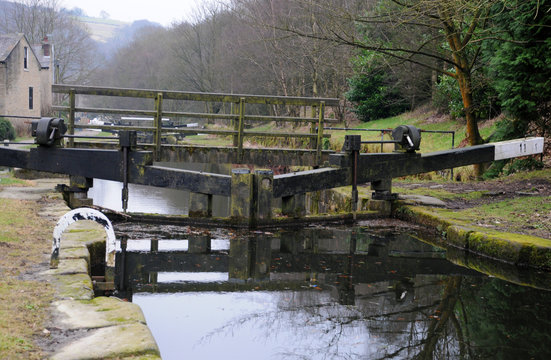 set of lock gates on a canal with wooden footbridge with dark water reflecting the trees and landscape near hebden bridge