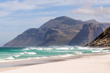 Fototapeta na wymiar Beautiful view of mountains near Hout Bay, Cape Town, South Africa, seen from Noordhoek Long Beach. White sand beach and waves with spray. Noordhoek Beach is a popular tourist destination.