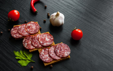 Tasty appetizer sandwich of thinly sliced spicy salami on bread on a dark wooden background