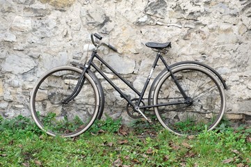 Old bike standing on grass in front of old stone wall