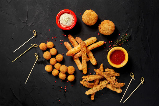 Allsorts of fried snacks with two different sauces on black background. Close-up. Top view