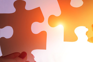 two hands trying to connect couple puzzle piece with sunset background. Jigsaw alone puzzle against...