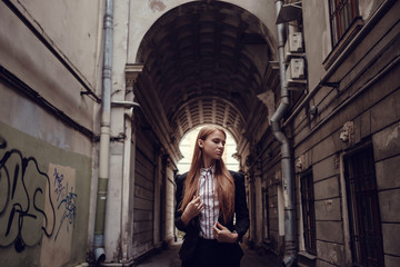 Fototapeta premium A young red-haired girl in a business suit is walking along a beautiful old town. St.Petersburg