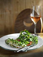 fish fillet with salad and a glass of rose wine on a wood table.
