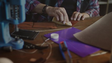 Leather worker polishing finished product. Leather manufacturer working with product in home workshop. Final processing leather goods at craft workshop