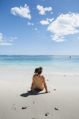 Fototapeta na wymiar Young woman looks at the horizon sitting on a beach of Mauritius Island in the summer