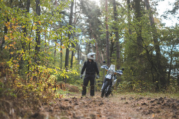 Obraz premium Man in dual sport helmet with backpack, enduro off road motorcycle on the forest road during sunrise. travel freedom concept