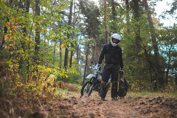 Man in dual sport helmet with backpack, enduro off road motorcycle on the forest road during sunrise. travel freedom concept