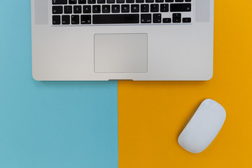 Laptop computer keyboard with mouse on bright yellow and blue background with copy space