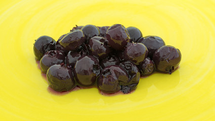 A small serving of canned blueberries in light syrup on a bright yellow plate.