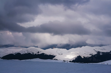 Beautiful view of the winter ski resort. Mountains with clouds, in the distance ski lift.
