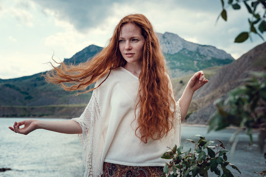 Beautiful boho styled model wearing white crochet swimsuit posing on the beach in sunlight