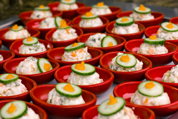 Portion salad with mayonnaise in a red plate, decorated with a piece of cucumber