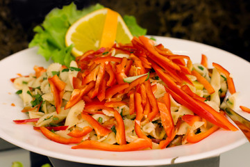 Salad of pasta with sweet red pepper, decorated with lemon and lettuce leaves